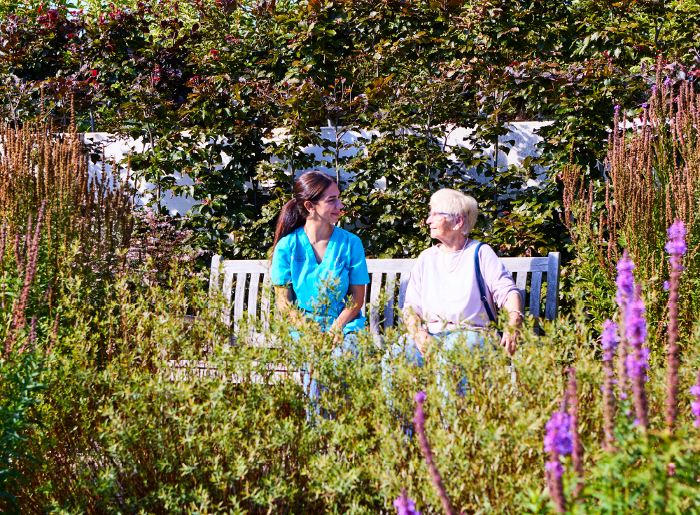 Pflegekraft und Bewohnerin auf einer Bank im Park des WohnGut Osterseifen