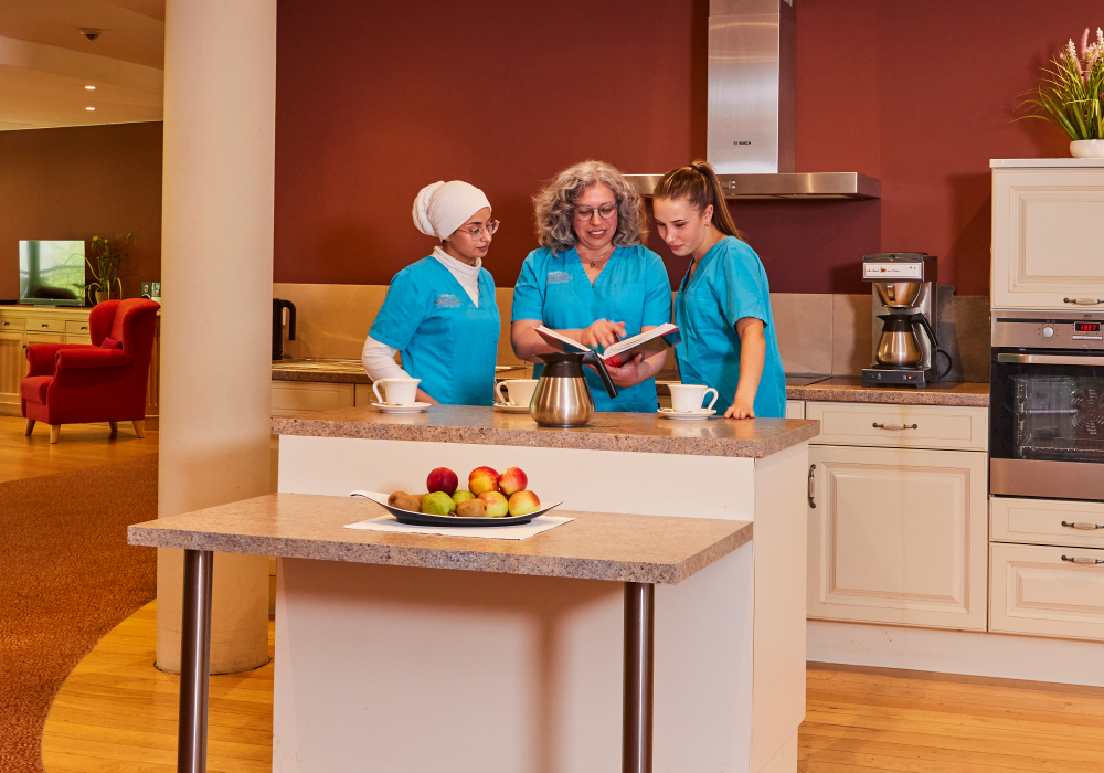 Pflegekräfte mit aufgeschlagenem Buch in der Wohnküche im WohnGut Saalhausen